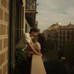 a man and woman kissing on top of a balcony overlooking the cityscape with buildings in the background