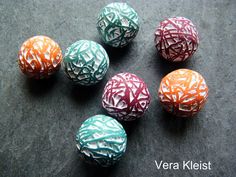 six different colored balls with white and orange designs on them sitting on a black surface