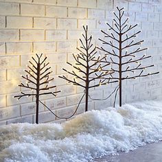 three small trees are in the snow near a brick wall with lights on each side