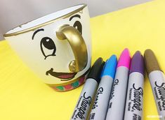 four crayons sitting next to a coffee cup with face drawn on the side