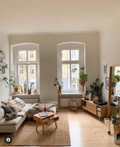 a living room filled with furniture and lots of windows next to a wooden floor covered in potted plants