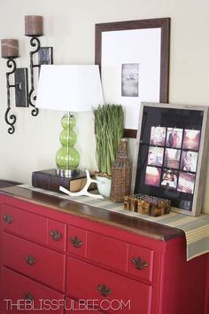 a red dresser with pictures on the top and two green vases next to it