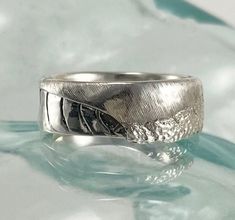 a silver ring sitting on top of a blue glass table next to a white background