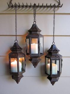 three hanging lanterns with lit candles in them on the side of a house or building