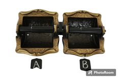 two black and gold metal objects with letters in the middle, one has a letter on it