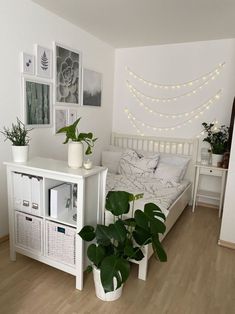 a white bedroom with plants and pictures on the wall