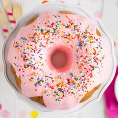 a pink frosted donut with sprinkles in a white cake pan