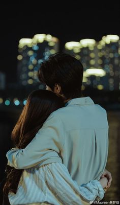 a man and woman embracing each other in front of a cityscape at night