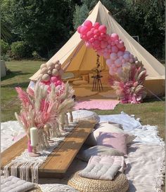 a tent set up for a party with pink and white balloons on the ceiling, pillows in front of it