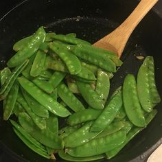 green beans are being cooked in a skillet with a wooden spoon on the side