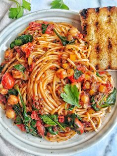 a white plate topped with pasta and spinach covered in tomato sauce next to grilled cheese