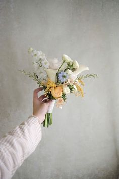 a person holding a bouquet of flowers in their hand with white and yellow flowers on it