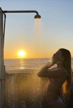 a woman standing under a shower head next to the ocean