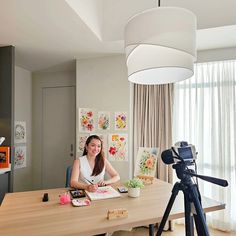 a woman sitting at a table with a camera in front of her and some pictures on the wall