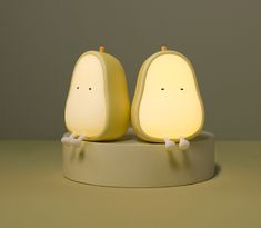 two pear shaped lights sitting on top of a white stand with one light turned on