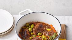 a pot filled with meat and vegetables on top of a wooden cutting board next to a plate