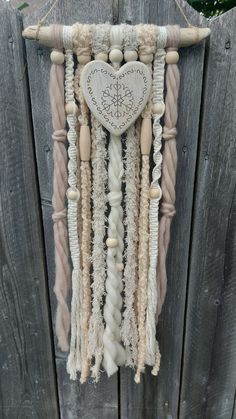 a heart hanging on the side of a wooden fence with rope and beads attached to it