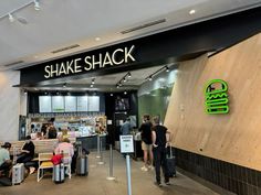 people are sitting at tables in front of the shake shack sign and entrance to an eatery