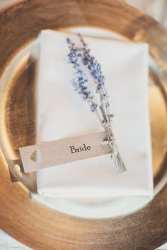 a place setting with napkins and lavender flowers on it, as well as a name tag