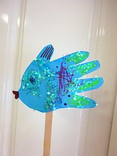 a handprinted blue fish on a stick in front of a white door,