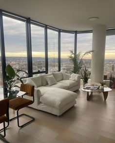 a living room filled with furniture and large windows overlooking the cityscape in the distance