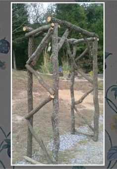 a wooden structure made out of sticks and logs in the middle of a field with trees behind it