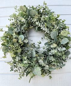 a wreath with green leaves and greenery hanging on the side of a house wall