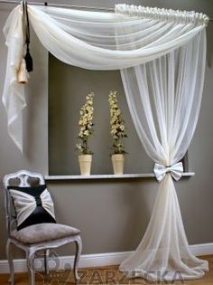 a chair sitting in front of a window covered with sheer curtains and flower vases