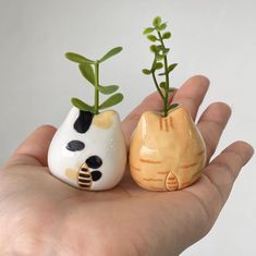 two small ceramic animals sitting on top of each other's palms with plants growing out of them