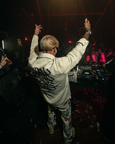 a dj in front of a crowd at a party with his hands up to the air