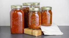 four jars of tomato sauce sitting on top of a wooden block next to a napkin