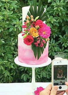 a person taking a photo of a pink cake with flowers on it and a cell phone