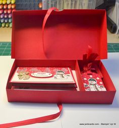 an open red box on a table with some cards in it and a ribbon around the bottom