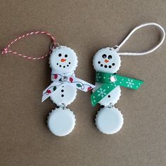 two snowman ornaments are hanging on a string with a green and white ribbon around them