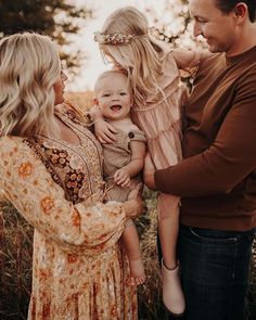 a man and woman holding a baby while standing next to each other in a field