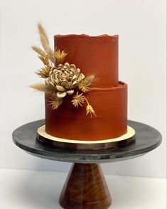 a three tiered red cake with gold accents on a black plate and wooden stand