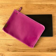 a pink purse sitting on top of a wooden floor next to a black folder and pen