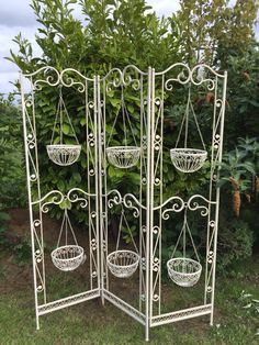 three white metal plant stands with baskets on them in front of some bushes and trees