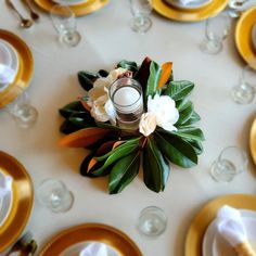 an arrangement of flowers and candles on a white table cloth with gold rimmed plates