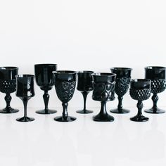 black glass goblets are lined up on a white surface, with one in the middle