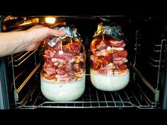 two jars filled with food sitting inside of an oven, being held by someone's hand