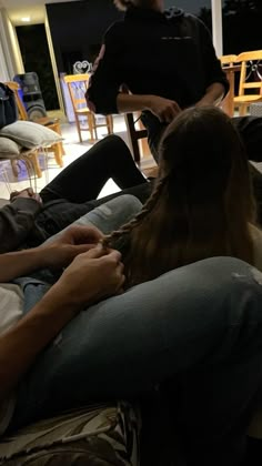 two people sitting on a couch with one person cutting another persons hair in the background