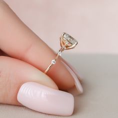 a woman's hand holding a ring with a diamond on it and a pink manicure