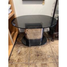 a glass table with a metal basket underneath it on a tile floor in front of a white wall