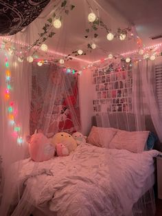 an unmade bed with lights hanging from the ceiling and stuffed animals on the pillows