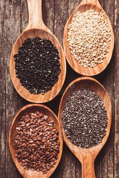 four wooden spoons filled with different types of seeds on top of a wooden table