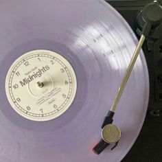 a purple record with a clock on the side and a stick sticking out of it