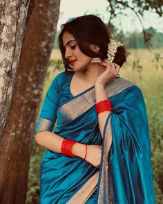 a woman in a blue sari standing next to a tree