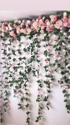 pink and white flowers are hanging from the side of a wall with greenery on it