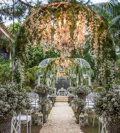 an outdoor ceremony setup with white chairs and greenery on the ground, surrounded by trees